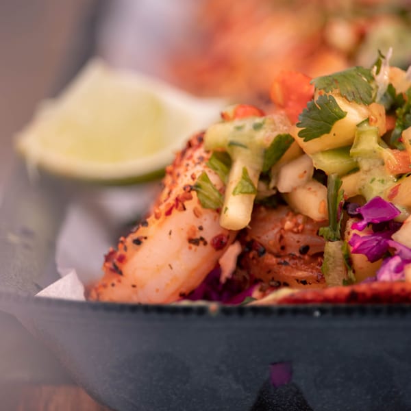 Close-up of a Machetes Gourmet shrimp taco with pineapple salsa and a lime wedge.