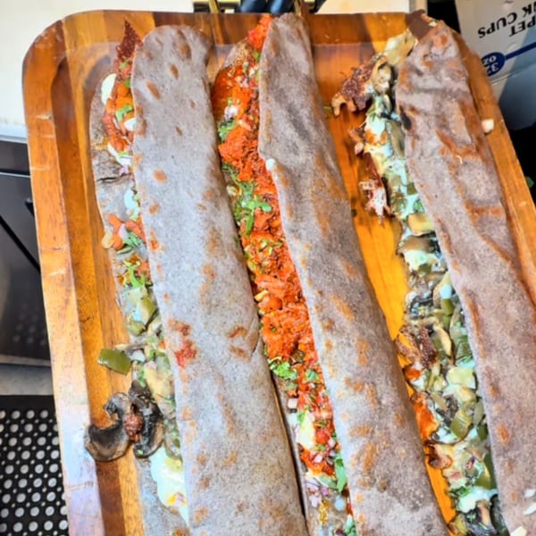Three long, folded Machetes Gourmet tortillas filled with various Mexican ingredients on a wooden tray.